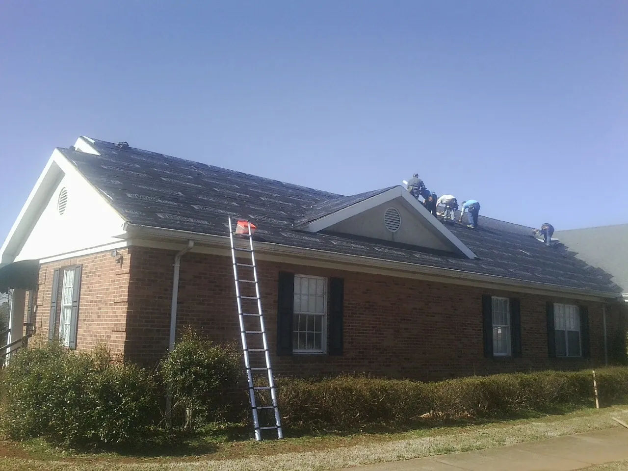 Crew tearing shingles off a brick ranch roof with a ladder set — Emergency Roof Repair work by our crew in Harpswell