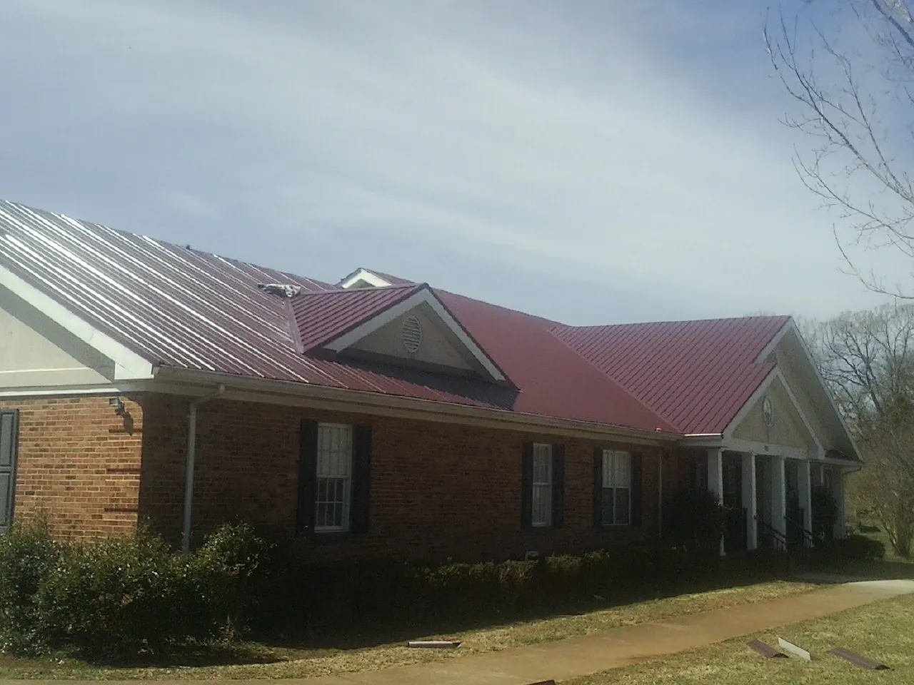 Red metal roof with gabled entries on a long brick building, from a Hail Damage Roof Repair job in Harpswell