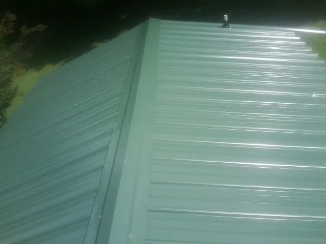 New green metal panels meeting at the ridge of a roof — Flat Roof Repair work by our crew in Harpswell