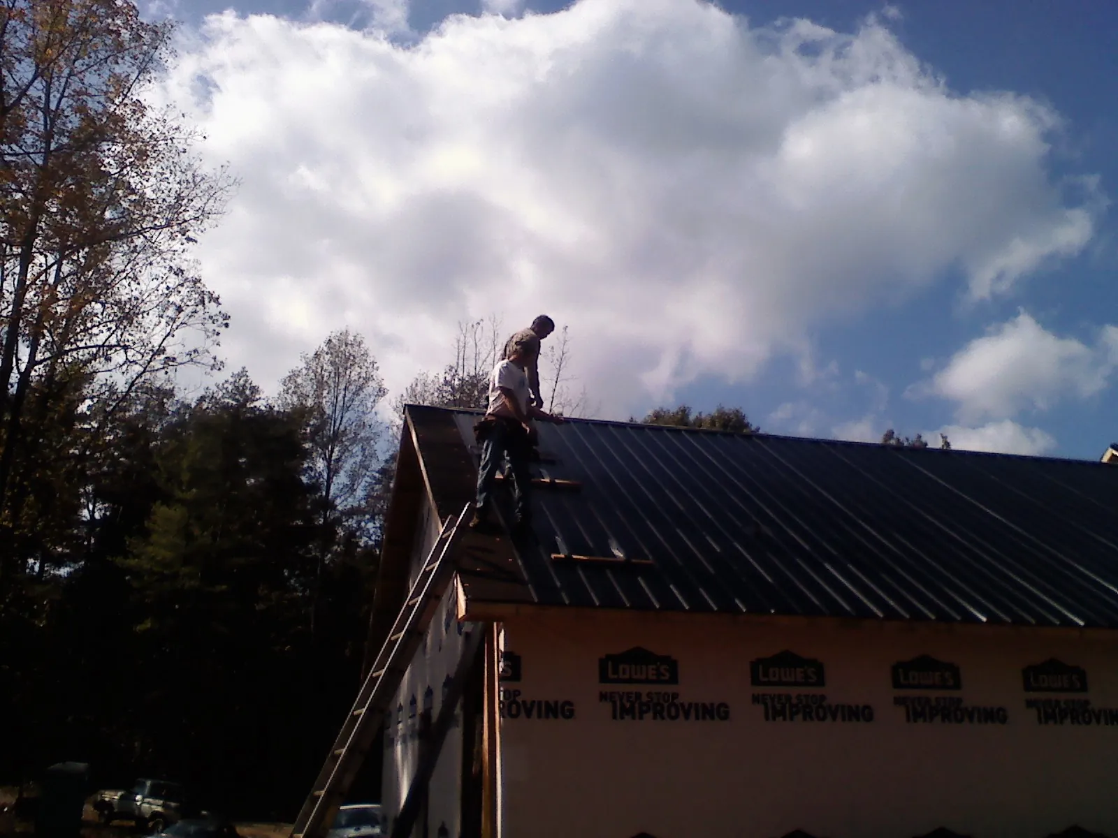 Roofer fastening dark metal panels high against a cloudy sky, from a Roof Inspection job in Harpswell