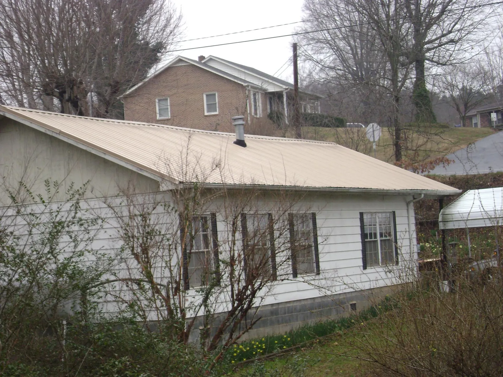 Tan metal roof on a white sided house set into a hillside — Commercial Roofing by Roofing Brothers in Harpswell